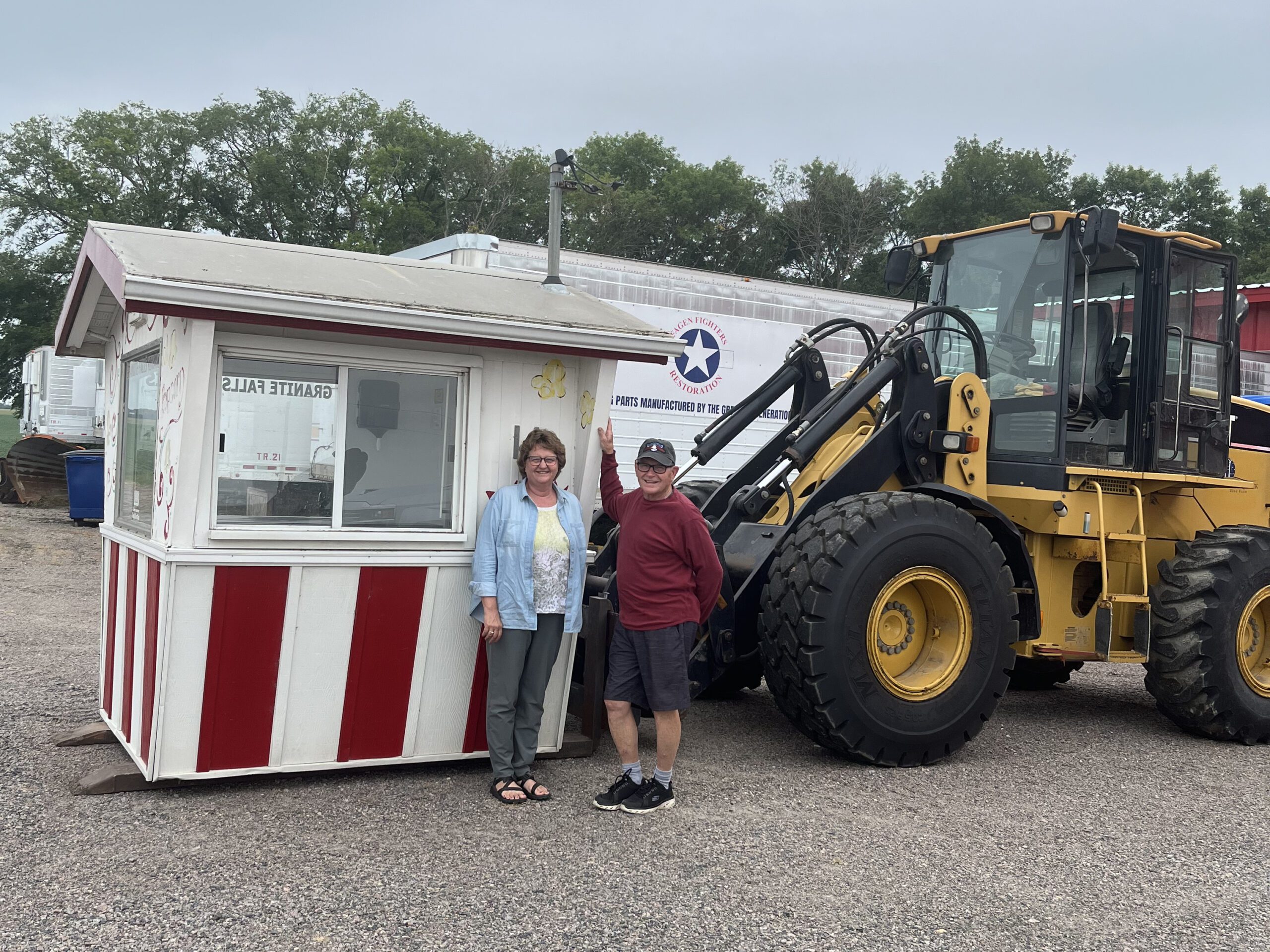 Judy and Tom in front of the popcorn box-shaped stand loaded onto the forks of a tractor attachment