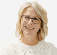 A smiling woman with light blonde hair, wearing glasses, a white textured sweater, and large brown earrings, against a plain white background.
