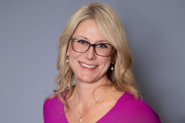 Claire Meyers poses for a formal head shot. She's wearing a magenta blouse and glasses.