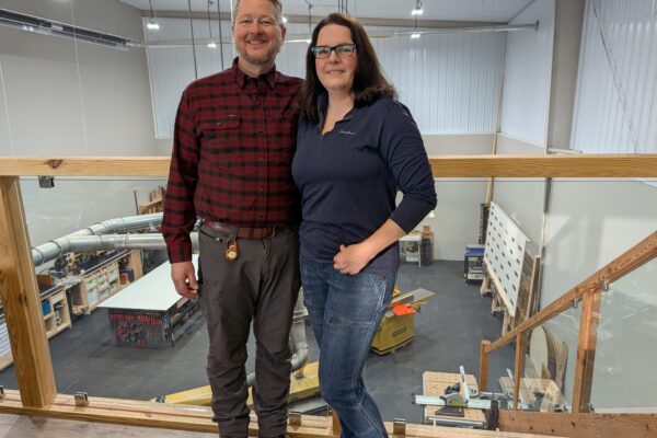 Kevin and Anne Veldhuisen stand on a balcony overlooking the shop for Woodgrain Custom Builds.