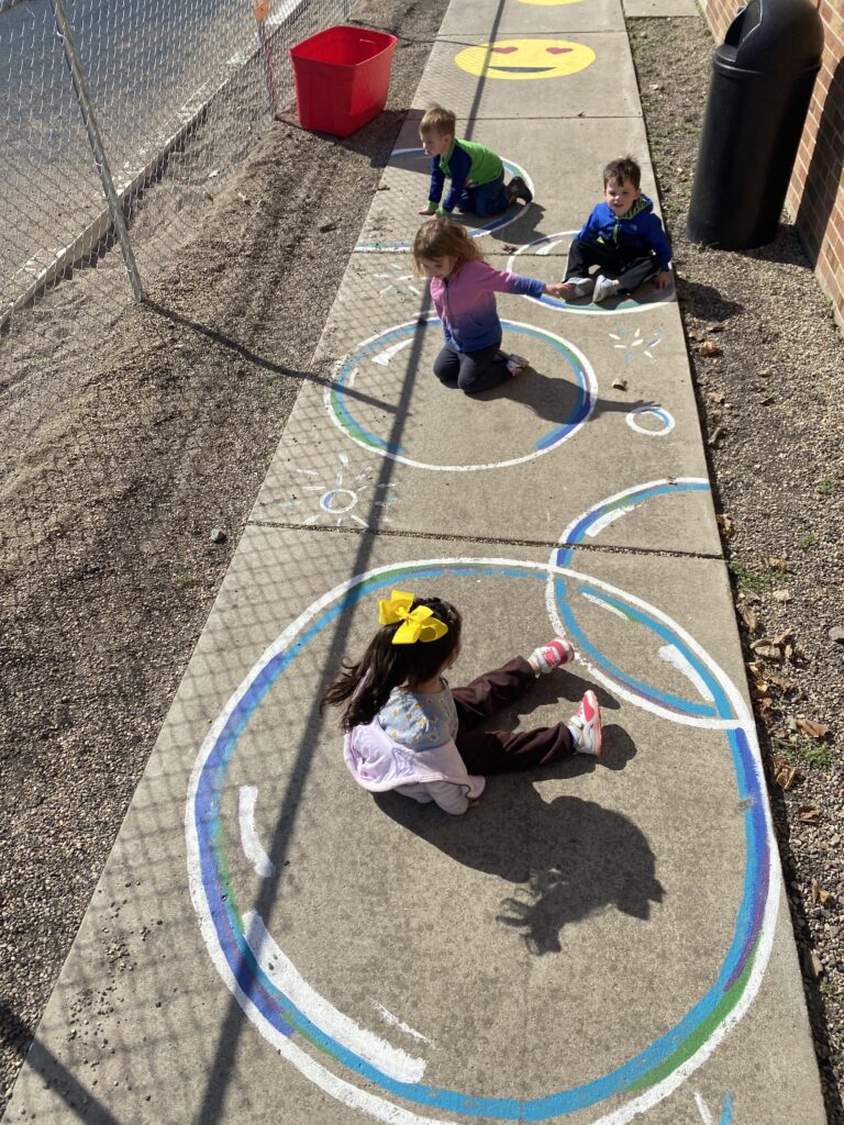 Children sit inside the outline of bubbles painted on the sidewalk as part of the Born Learning Trail in Madison.