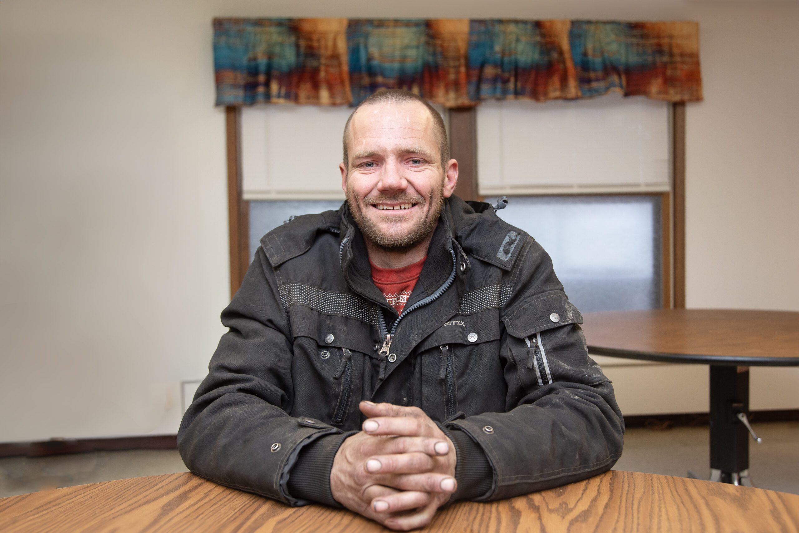 Mark Stewart sits with his hands clasped in front of him on a round wooden table.
