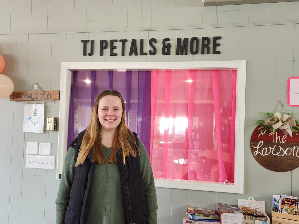 Trenna stands inside her small business with TJ Petals & More visible above her on the wall.