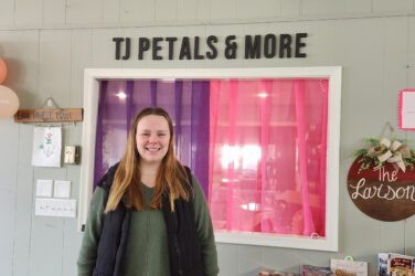Trenna stands inside her small business with TJ Petals & More visible above her on the wall.