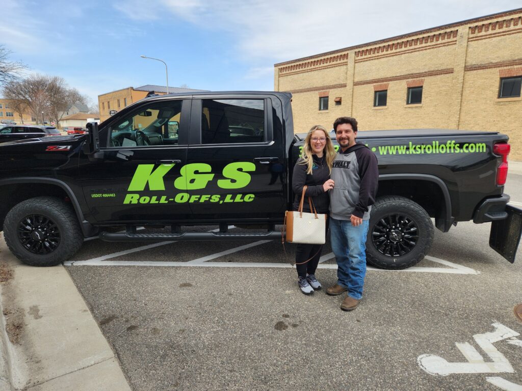 Kyle and Sommer Harris pose outside next to a pick-up truck with K&S Roll-Off’s logo on the side.
