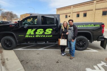 Kyle and Sommer Harris pose outside next to a pick-up truck with K&S Roll-Off’s logo on the side.