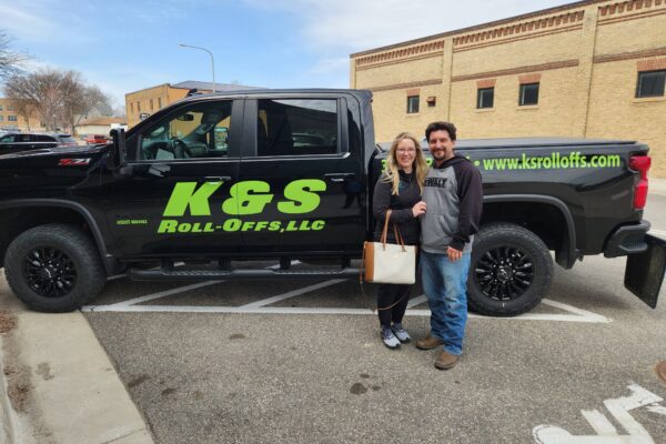 Kyle and Sommer Harris pose outside next to a pick-up truck with K&S Roll-Off’s logo on the side.