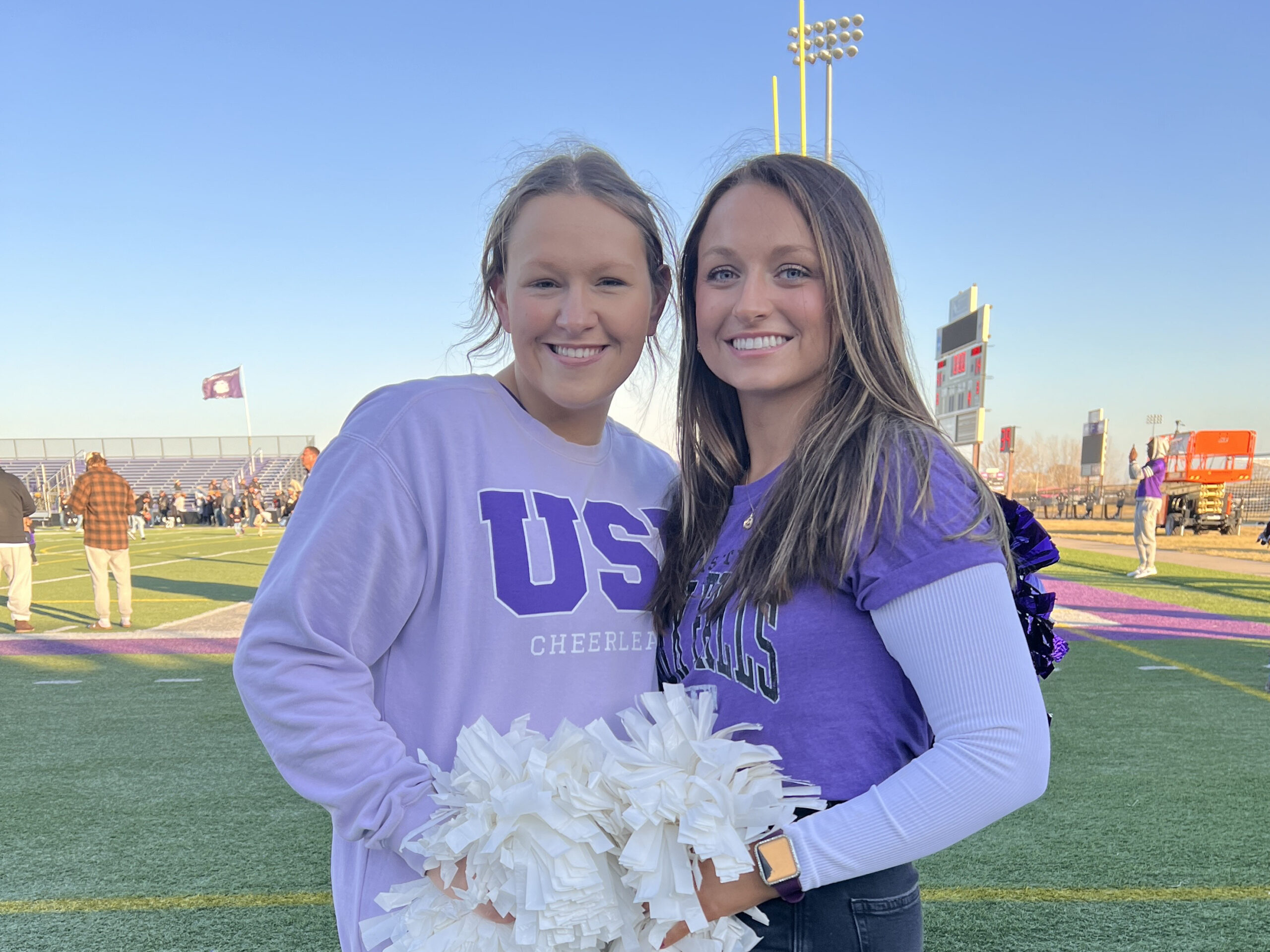 Scholarship recipients Morgan and Ashlyn are decked out in school spirit wear and hold white pom-poms.