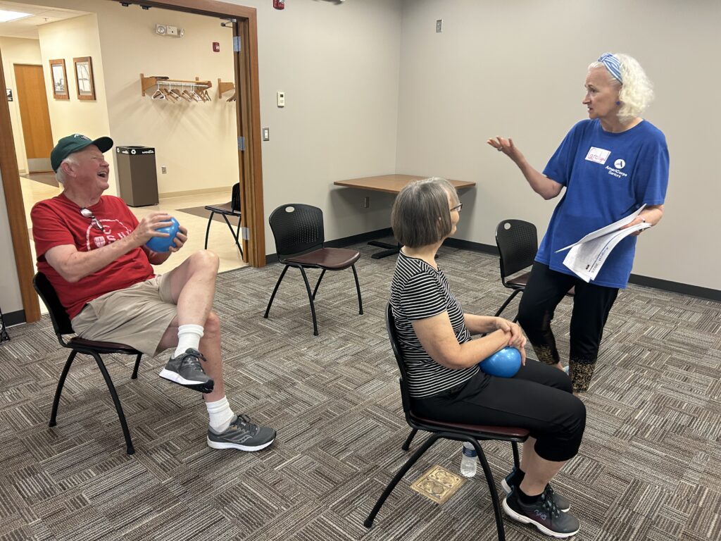Carolyn holds papers in her hand and talks to a couple participants in Winsted SAIL classes.
