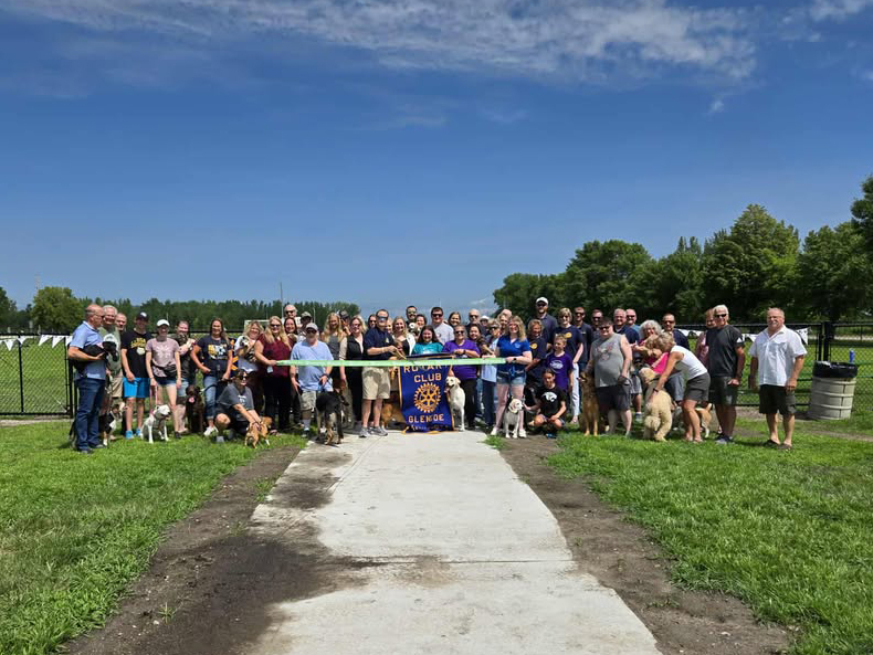 A large group is assembled for the ribbon cutting at the new Glencoe Rotary Dog Park on a sunny day.