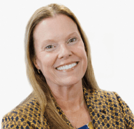 Stacy has straight light brown hair and is wearing a patterned blazer over a blue top, posed in front of a plain white background smiling.