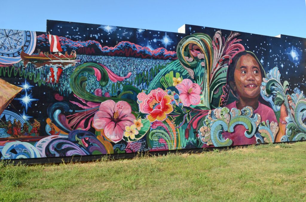 Colorful mural featuring a smiling girl, vibrant flowers, swirling waves, and a canoe with a red sail, set against a starry night sky.
